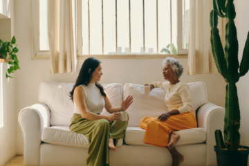 Two women talking to each other while sitting on a couch